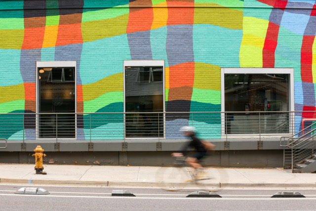 Cyclist riding past a colorful urban mural in Colorado